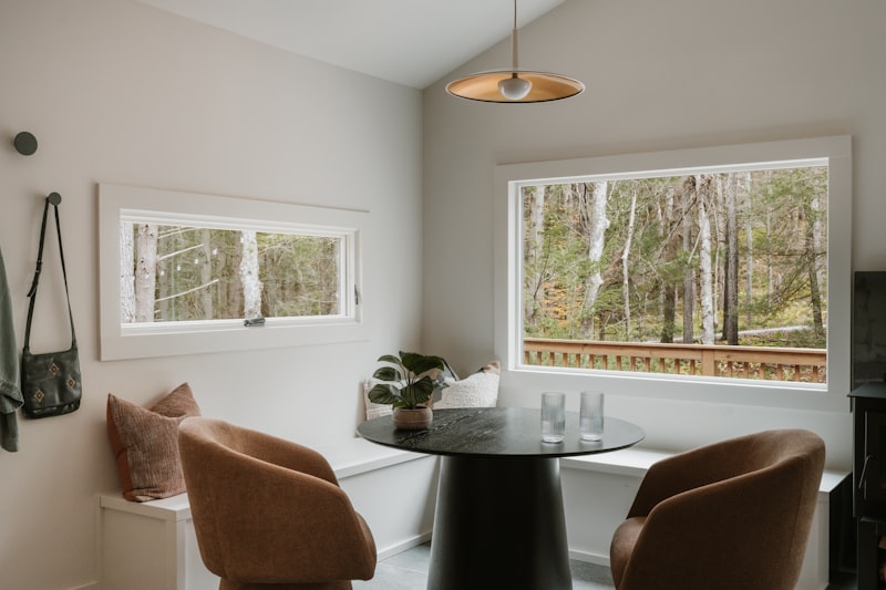 Corner window banquette with cushions and a round pedestal table, two armchairs opposite