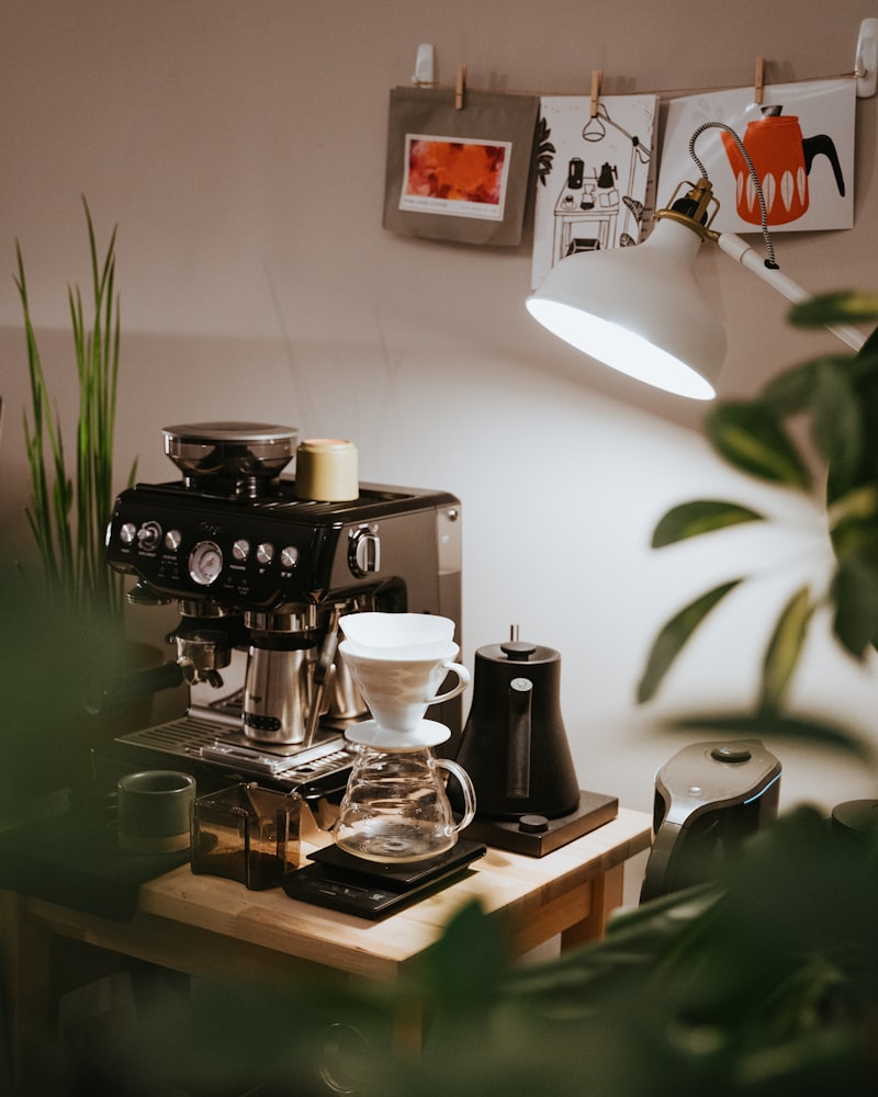 Home coffee station on a small wooden table: espresso machine, pour-over dripper on a scale, and a gooseneck kettle