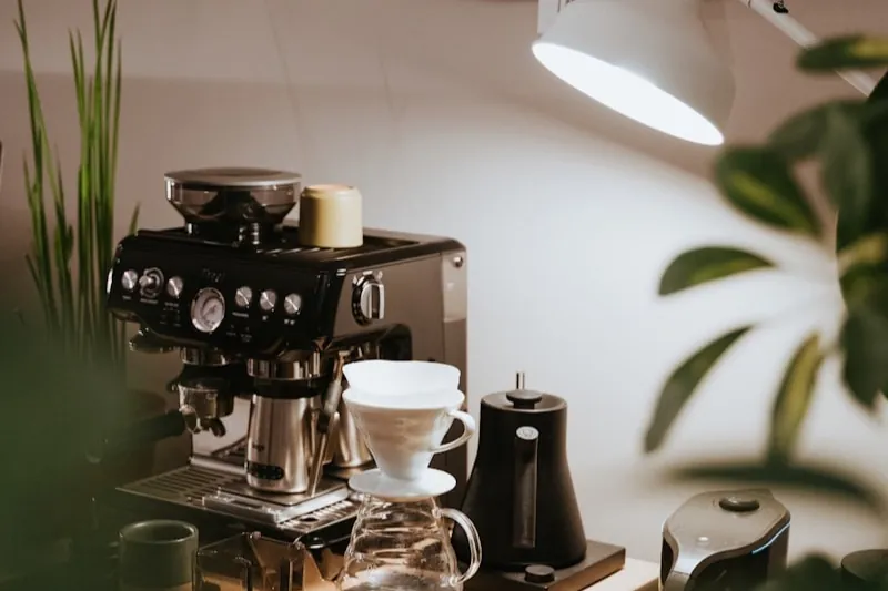 Home coffee station on a small wooden table: espresso machine, pour-over dripper on a scale, and a gooseneck kettle