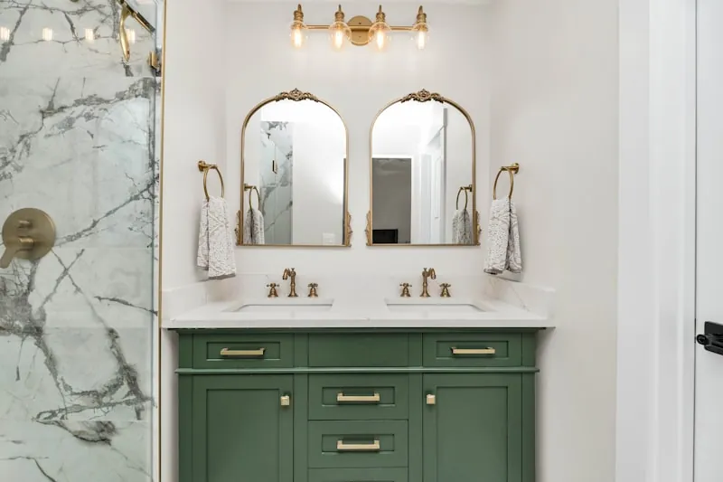 Green Shaker double vanity with brass hardware beside a marble shower surround