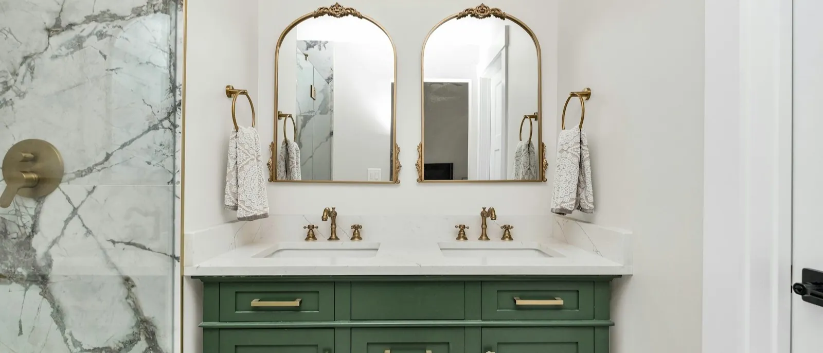 Green Shaker double vanity with brass hardware beside a marble shower surround