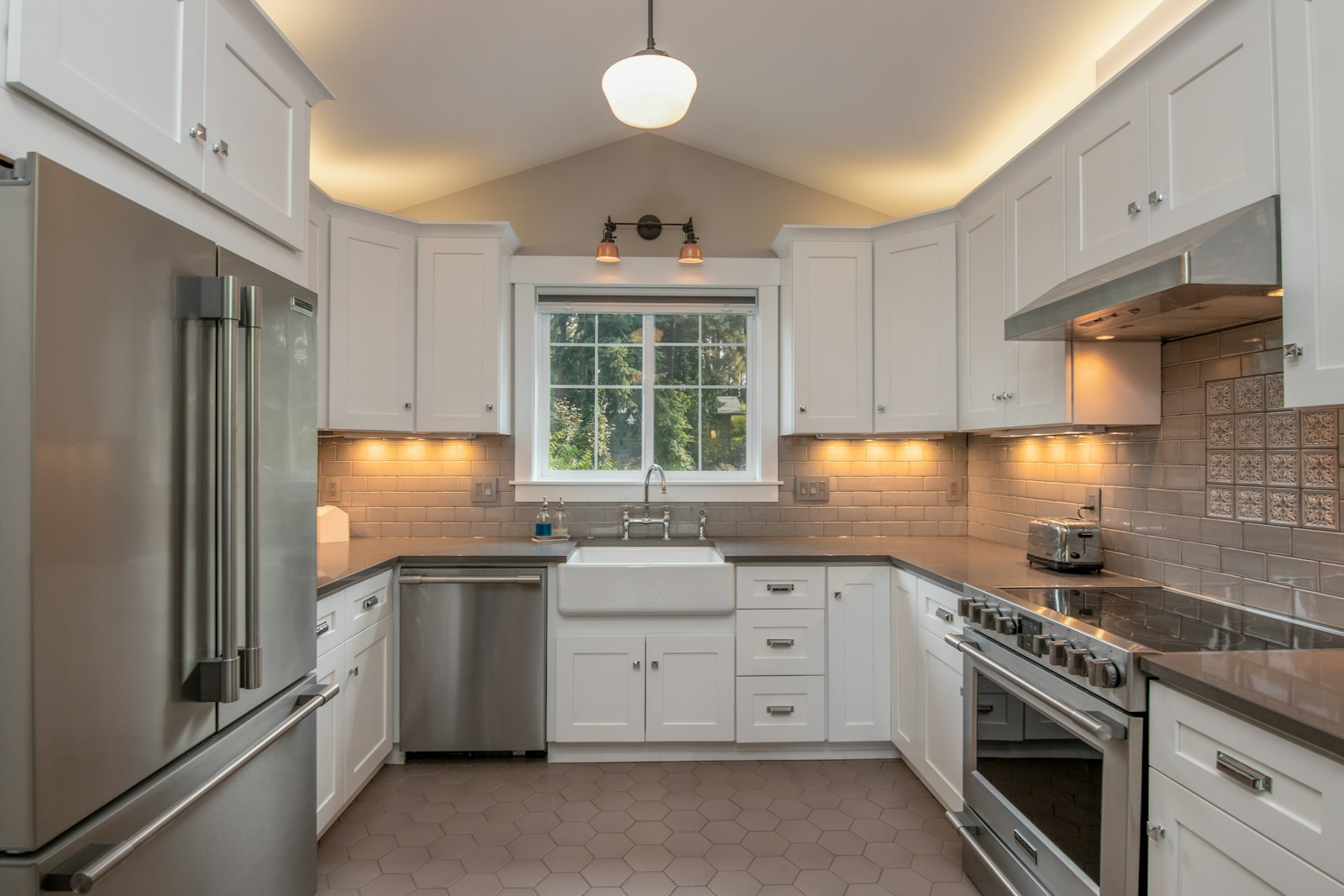 White Shaker kitchen with a farmhouse apron sink under a window, stainless range and refrigerator
