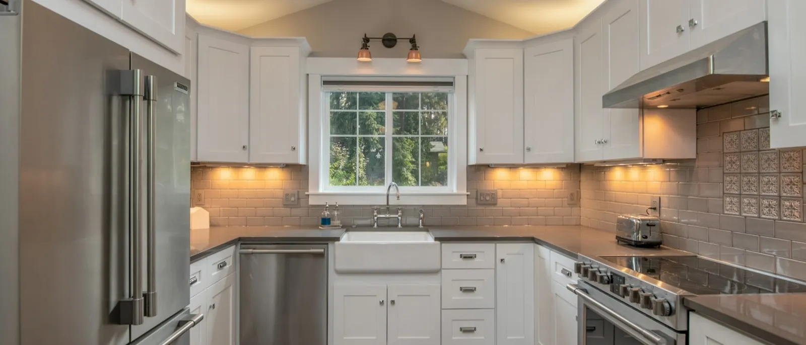 White Shaker kitchen with a farmhouse apron sink under a window, stainless range and refrigerator