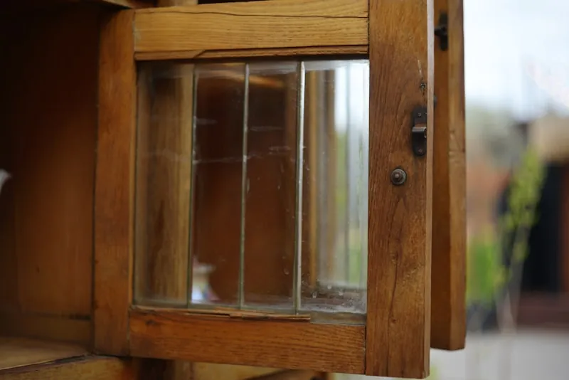 Close-up of a glazed wooden cabinet door standing open on its latch