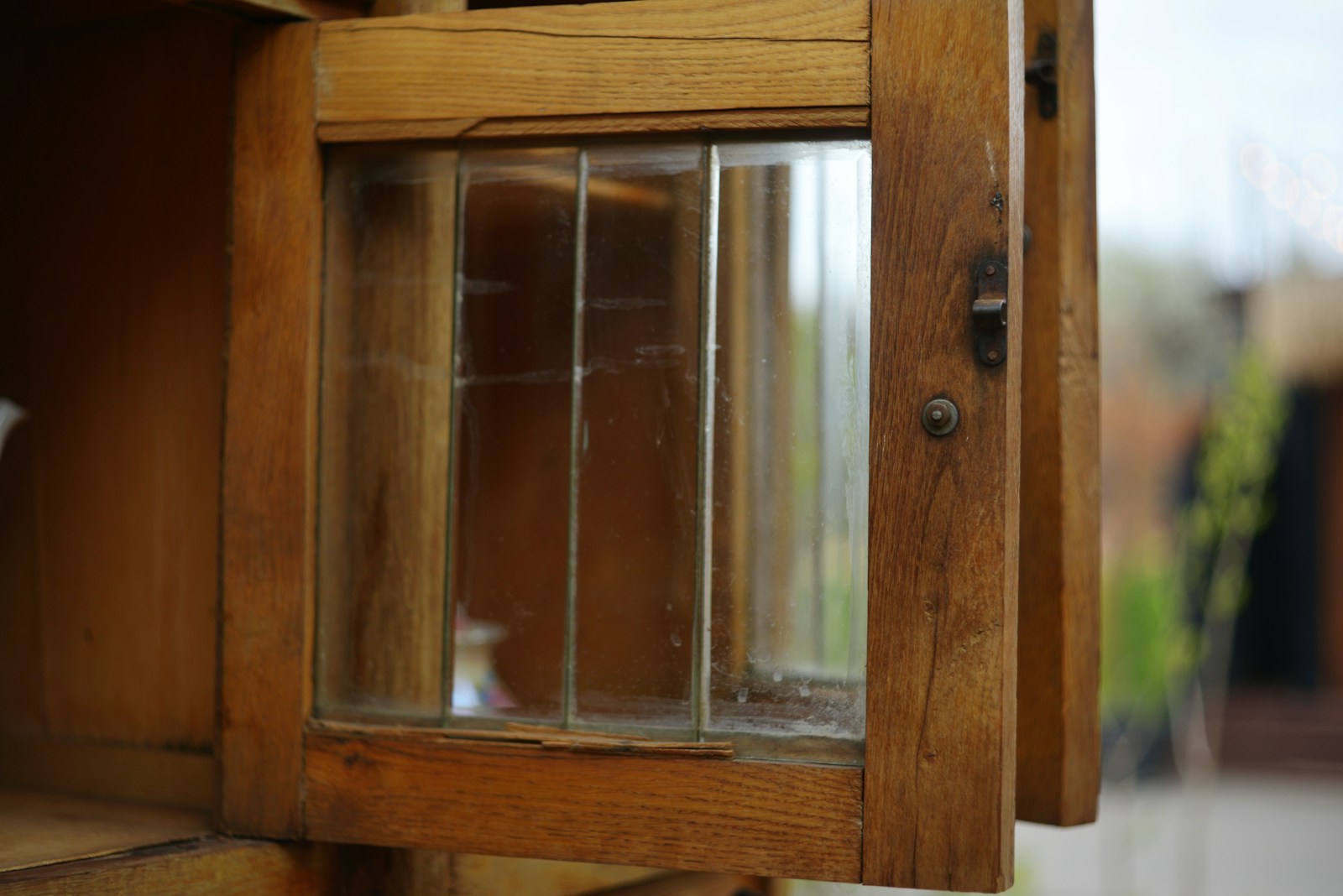 Close-up of a glazed wooden cabinet door standing open on its latch