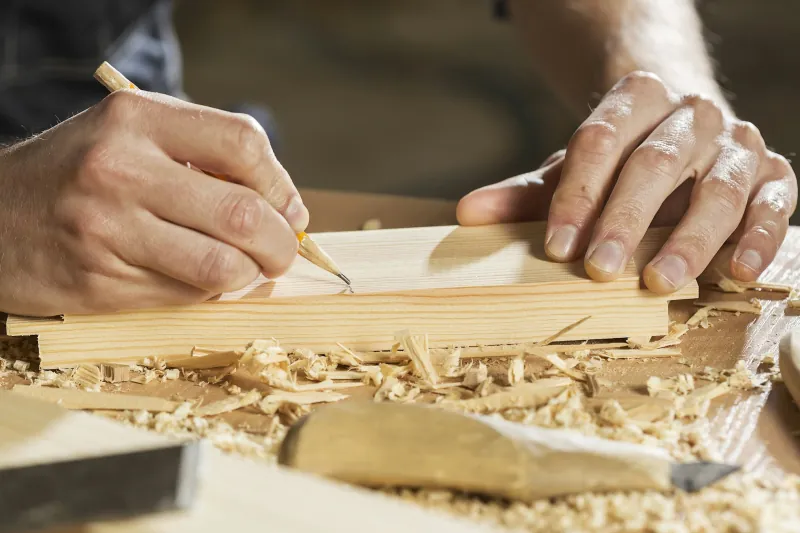 Photo of hands marking a pine board with a pencil on a workbench.