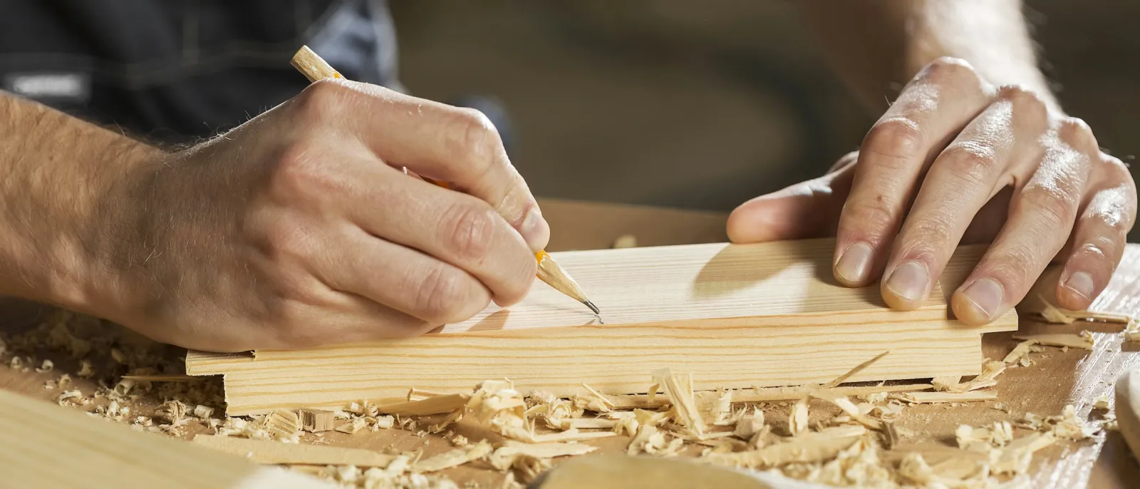 Photo of hands marking a pine board with a pencil on a workbench.