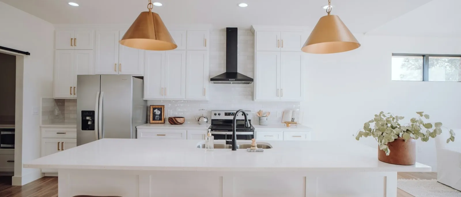 White Shaker kitchen island with a sink, brass pendant lights, and four leather counter stools