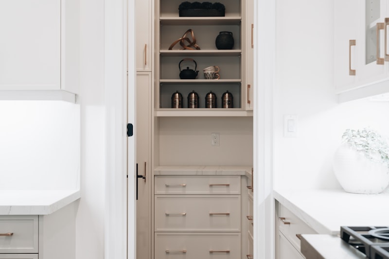 Narrow pantry cabinet seen through a doorway, open shelves of canisters above and drawers below