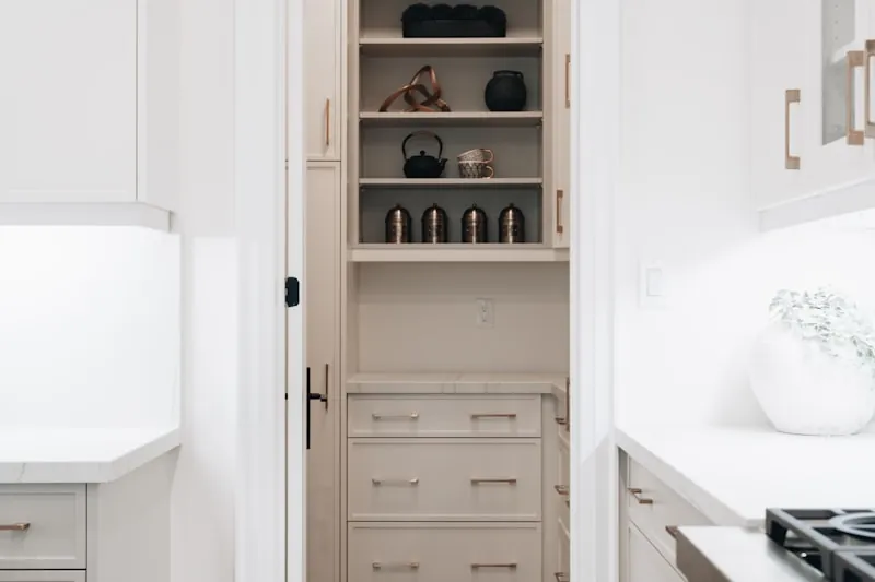 Narrow pantry cabinet seen through a doorway, open shelves of canisters above and drawers below