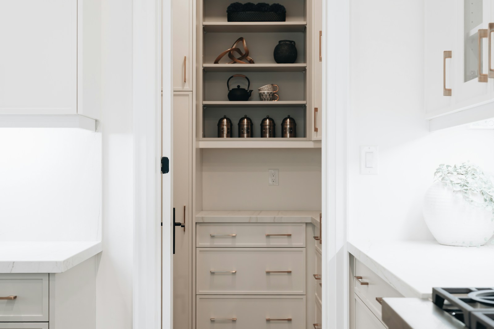 Narrow pantry cabinet seen through a doorway, open shelves of canisters above and drawers below