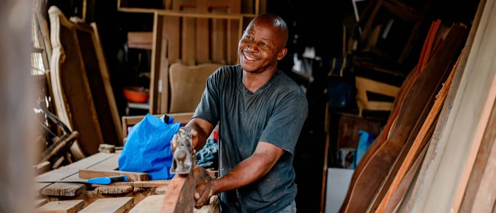 Woodworker smiling while shaping a board at a bench in a wood shop.