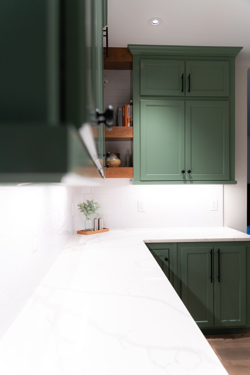Green-painted Shaker cabinets above a white marble counter, one door open to wooden shelves