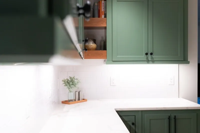 Green-painted Shaker cabinets above a white marble counter, one door open to wooden shelves