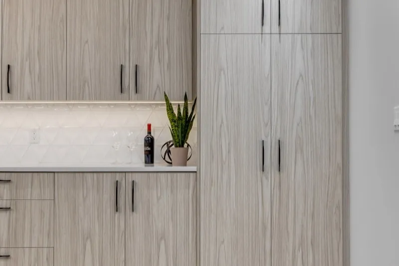 Pale wood-grain cabinets running floor to ceiling beside a white counter and tiled backsplash