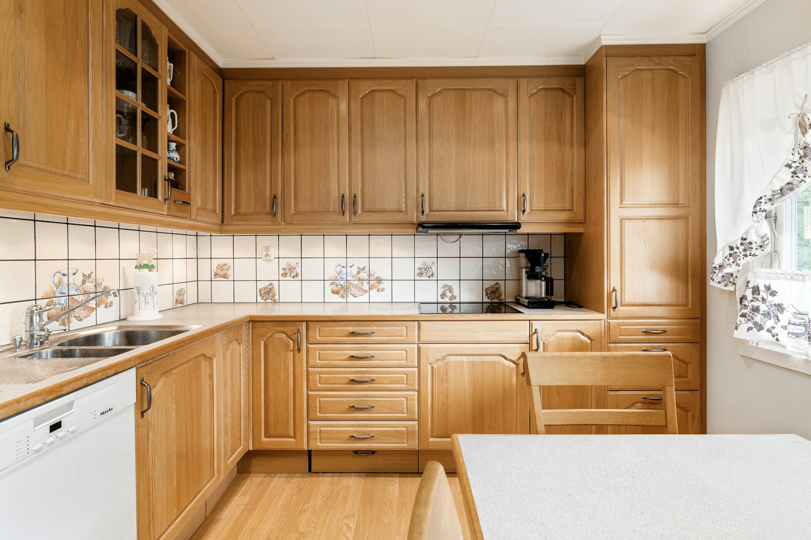 A kitchen fitted with oak cabinets, glass-front uppers, and a tiled backsplash over the counters