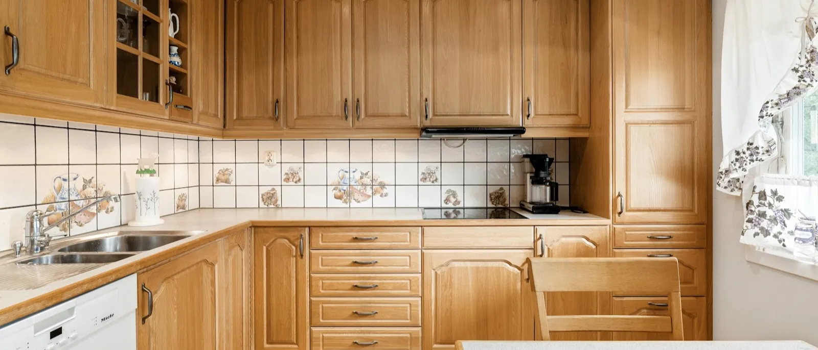 A kitchen fitted with oak cabinets, glass-front uppers, and a tiled backsplash over the counters